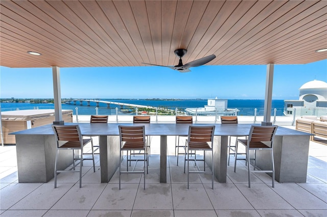 view of patio with exterior bar, a water view, and ceiling fan