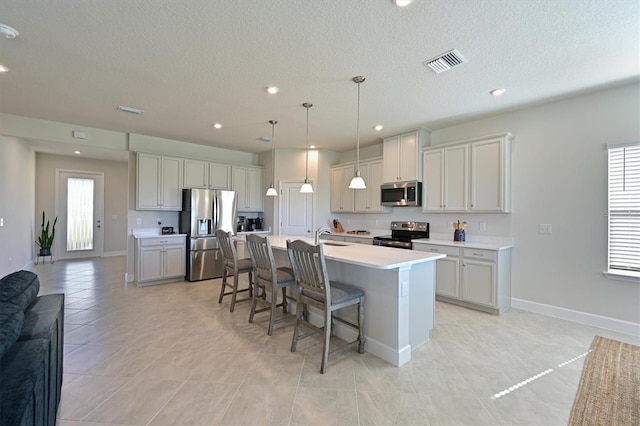 kitchen with stainless steel appliances, sink, decorative light fixtures, a breakfast bar area, and an island with sink