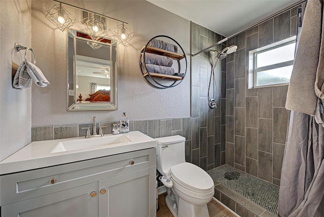 bathroom featuring ceiling fan, wood-type flooring, toilet, tiled shower, and vanity