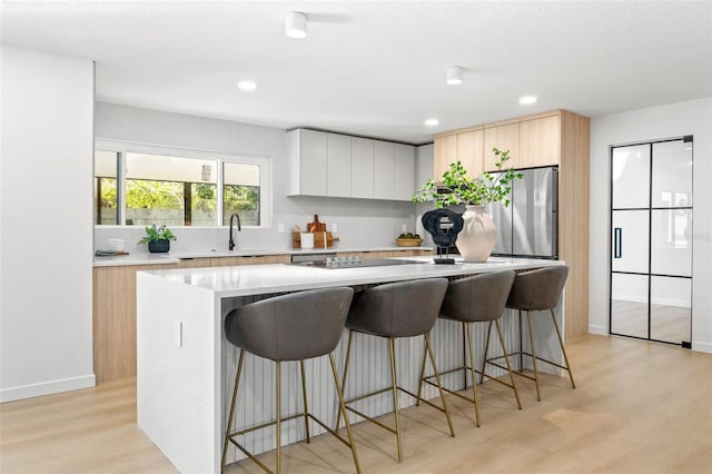 kitchen with a center island, black electric stovetop, light hardwood / wood-style flooring, a kitchen bar, and stainless steel refrigerator