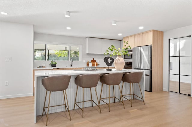 kitchen featuring light wood-type flooring, a textured ceiling, stainless steel appliances, white cabinetry, and a breakfast bar area