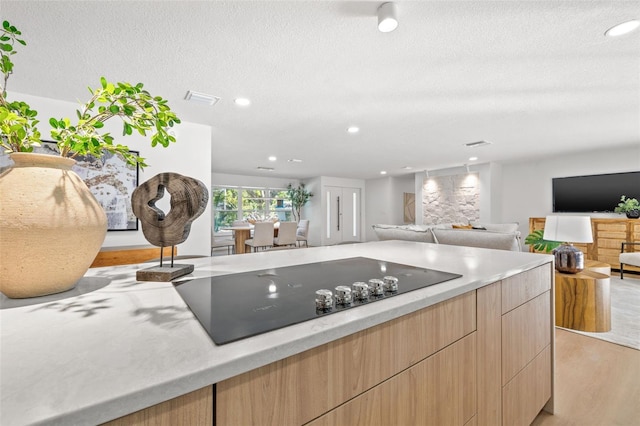 kitchen with light wood-type flooring, a textured ceiling, light brown cabinetry, and black electric cooktop