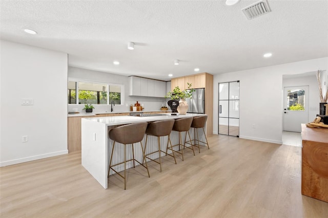 kitchen with stainless steel fridge, light wood-type flooring, a textured ceiling, a center island, and a breakfast bar area