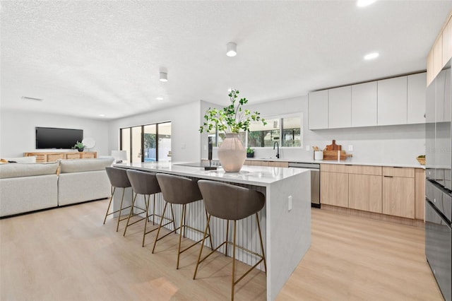 kitchen featuring white cabinetry, a kitchen island, stainless steel dishwasher, and light wood-type flooring