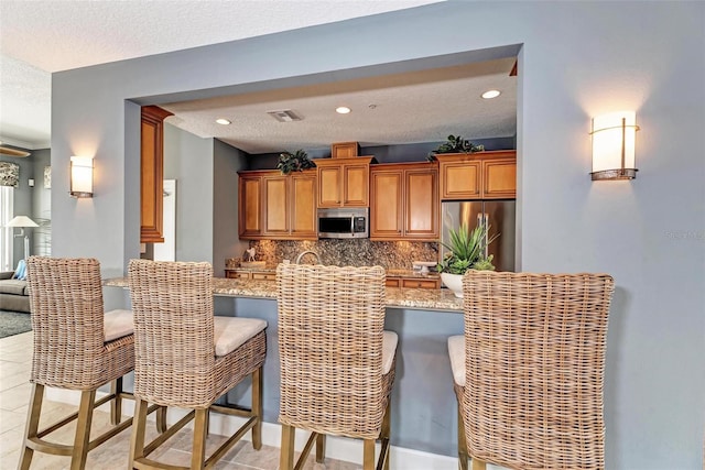 kitchen with light stone countertops, a textured ceiling, tasteful backsplash, light tile patterned flooring, and stainless steel appliances