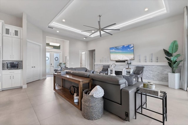 tiled living room with ceiling fan, a raised ceiling, and french doors