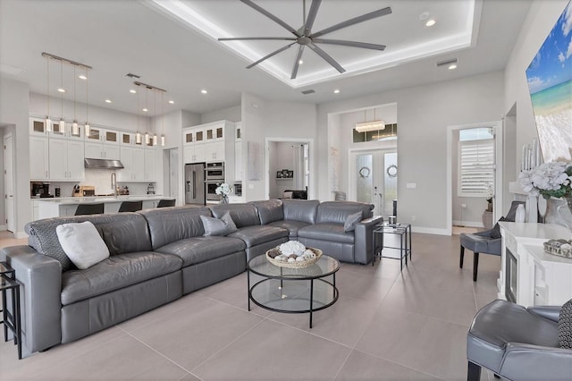 tiled living room featuring french doors, a raised ceiling, ceiling fan, sink, and a high ceiling