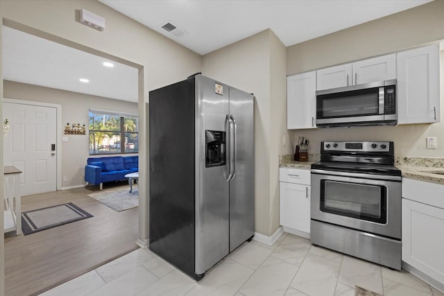 kitchen featuring white cabinets, light hardwood / wood-style floors, light stone countertops, and appliances with stainless steel finishes