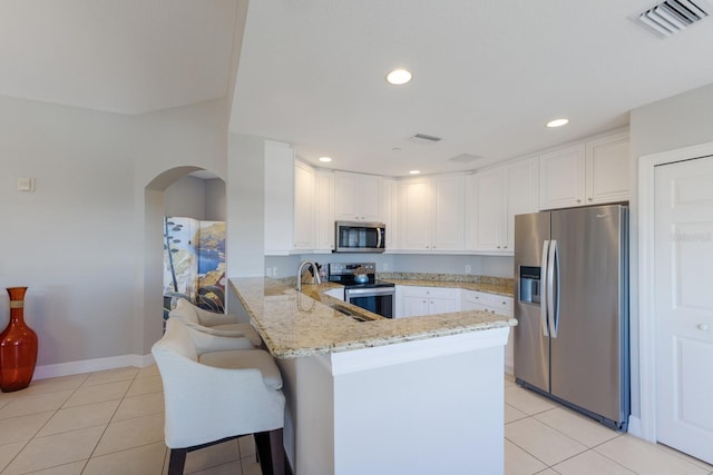 kitchen with white cabinetry, light stone counters, kitchen peninsula, a kitchen bar, and appliances with stainless steel finishes