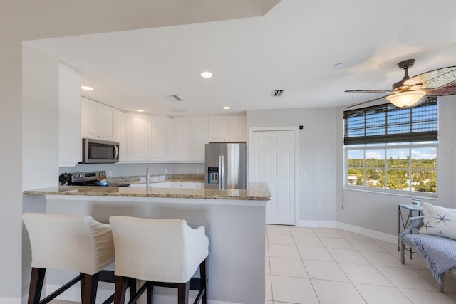 kitchen featuring a kitchen bar, kitchen peninsula, white cabinetry, and appliances with stainless steel finishes