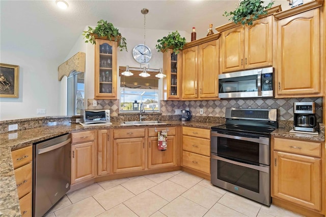 kitchen with appliances with stainless steel finishes, sink, dark stone countertops, hanging light fixtures, and light tile patterned flooring