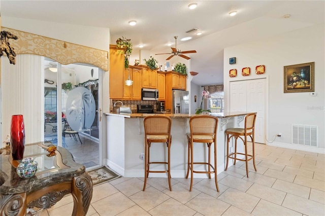 kitchen with vaulted ceiling, ceiling fan, appliances with stainless steel finishes, a kitchen bar, and kitchen peninsula