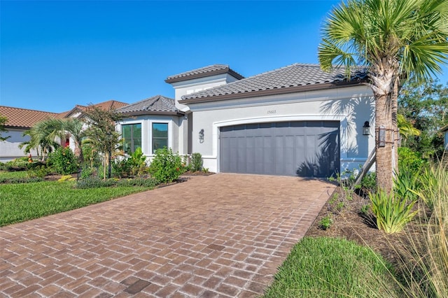 mediterranean / spanish-style house featuring decorative driveway, an attached garage, a tile roof, and stucco siding