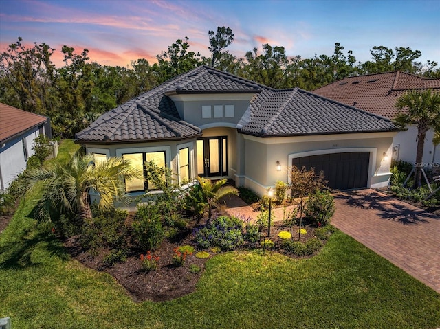 mediterranean / spanish house with a tile roof, stucco siding, decorative driveway, a yard, and a garage