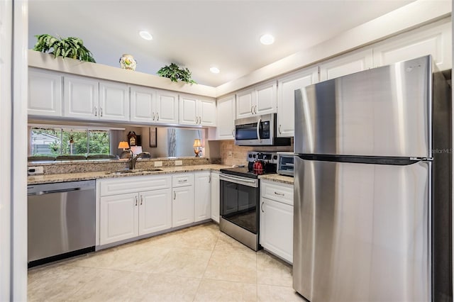 kitchen with white cabinets, sink, light tile patterned flooring, light stone counters, and stainless steel appliances