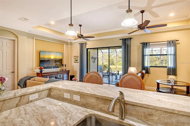 kitchen with ceiling fan, a raised ceiling, crown molding, and hanging light fixtures