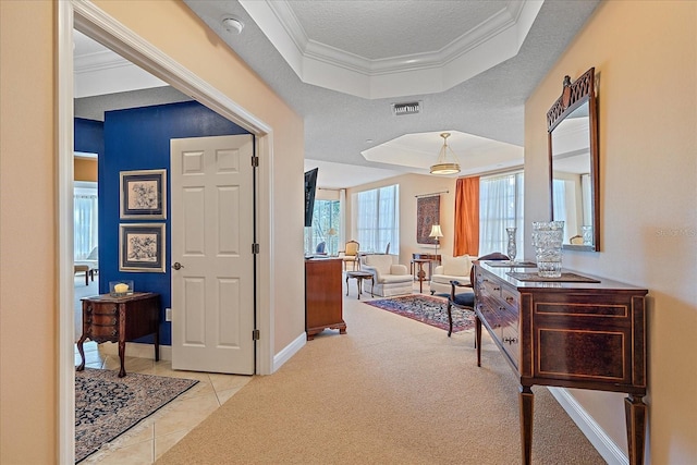 hall with a tray ceiling, crown molding, light colored carpet, and a textured ceiling