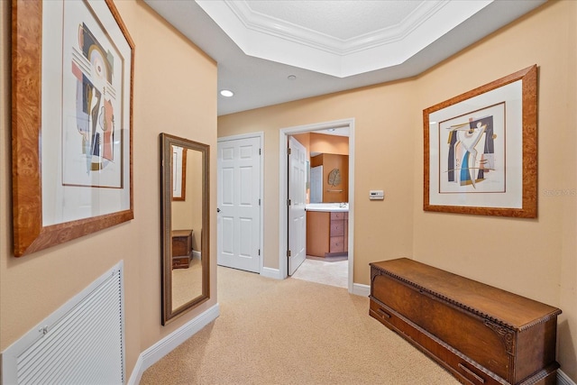 hallway with a raised ceiling, light colored carpet, and ornamental molding