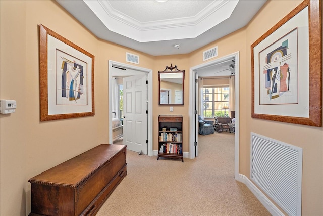 corridor with light colored carpet, ornamental molding, a textured ceiling, and a tray ceiling