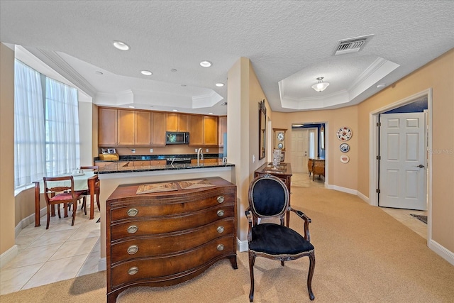 kitchen with kitchen peninsula, light carpet, dark stone counters, and a tray ceiling