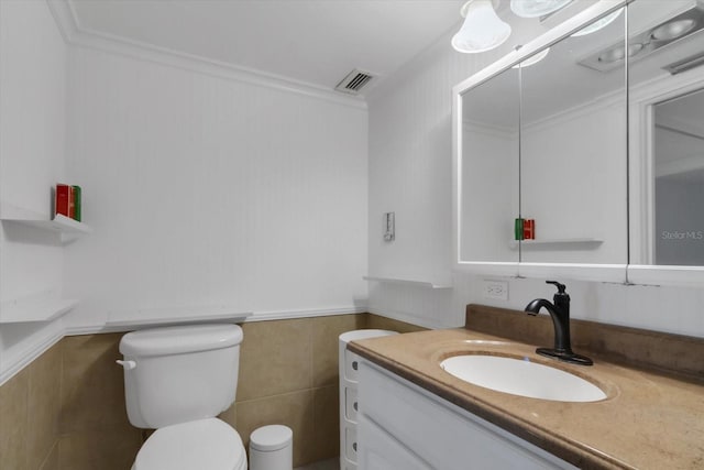 bathroom featuring vanity, toilet, crown molding, and tile walls