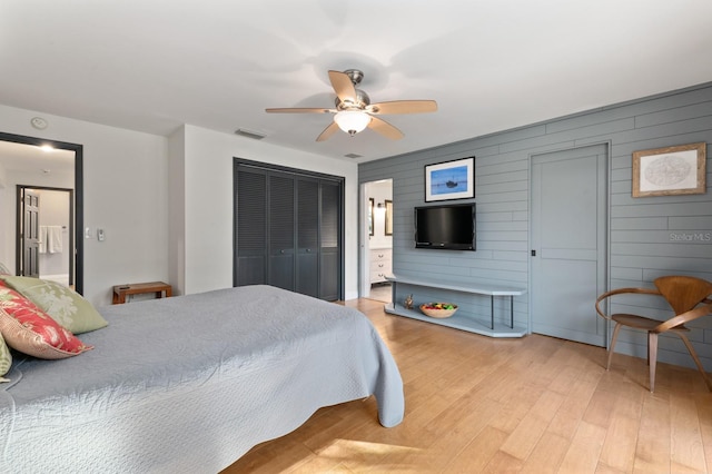 bedroom featuring ceiling fan, ensuite bathroom, light hardwood / wood-style floors, and wooden walls