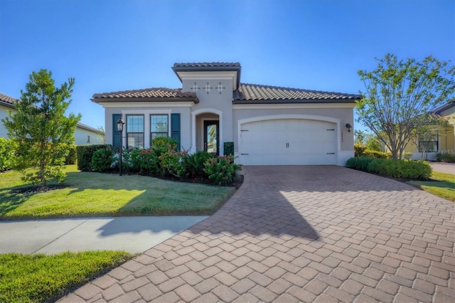 mediterranean / spanish-style home with an attached garage, a tile roof, decorative driveway, stucco siding, and a front lawn