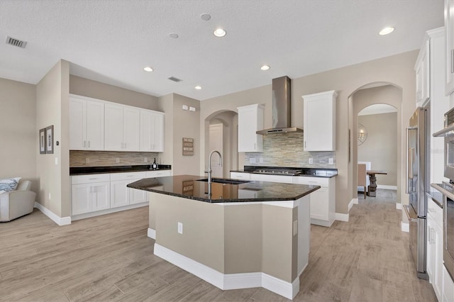 kitchen with white cabinetry, a center island with sink, wall chimney exhaust hood, and sink