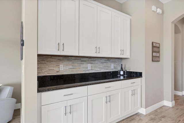 bar featuring white cabinets, light hardwood / wood-style floors, dark stone counters, and tasteful backsplash