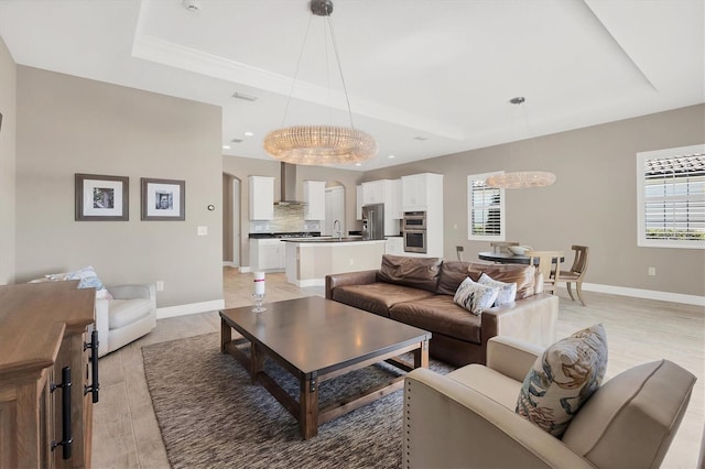 living room with light hardwood / wood-style floors, a raised ceiling, a notable chandelier, and sink