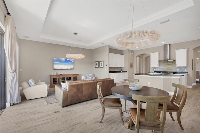 dining space featuring a chandelier, light wood-type flooring, a tray ceiling, and sink