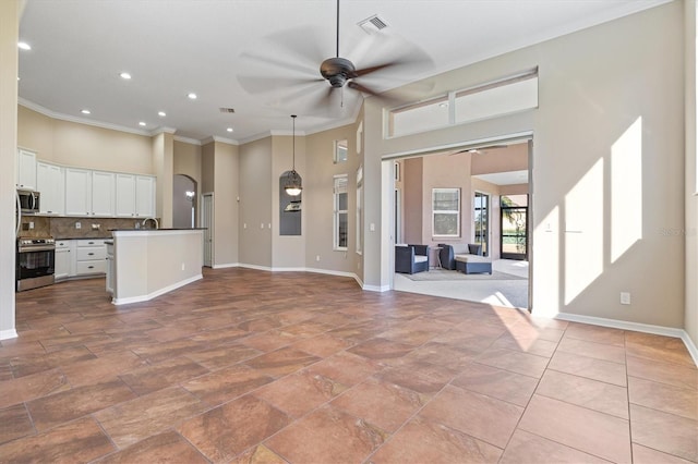 kitchen with ceiling fan, stainless steel appliances, tasteful backsplash, a center island with sink, and white cabinets