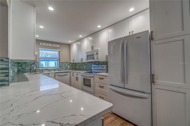 kitchen featuring tasteful backsplash, light stone counters, white appliances, sink, and white cabinetry