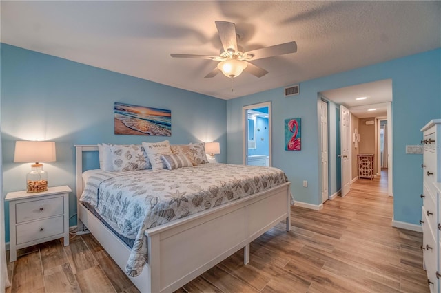 bedroom with ensuite bath, ceiling fan, light hardwood / wood-style floors, and a textured ceiling