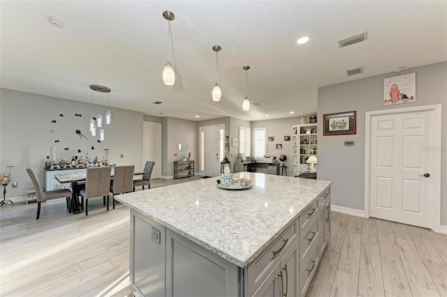 kitchen featuring light stone countertops, a center island, decorative light fixtures, light hardwood / wood-style floors, and gray cabinetry