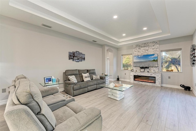 living room featuring a stone fireplace, a raised ceiling, and light hardwood / wood-style flooring