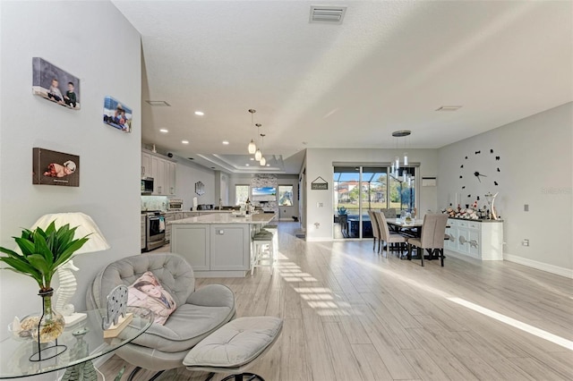 living room featuring baseboards, visible vents, a notable chandelier, and light wood finished floors