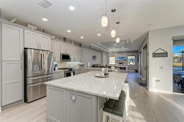 kitchen featuring a tray ceiling, a spacious island, visible vents, light wood-style flooring, and appliances with stainless steel finishes