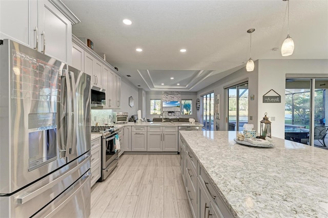 kitchen featuring a raised ceiling, light stone countertops, appliances with stainless steel finishes, light wood-style flooring, and recessed lighting