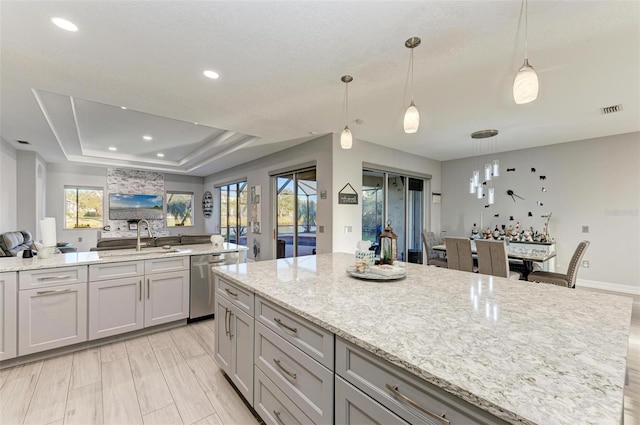 kitchen featuring visible vents, a sink, open floor plan, a tray ceiling, and stainless steel dishwasher