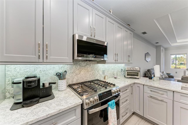 kitchen with light stone countertops, stainless steel appliances, open floor plan, gray cabinetry, and backsplash