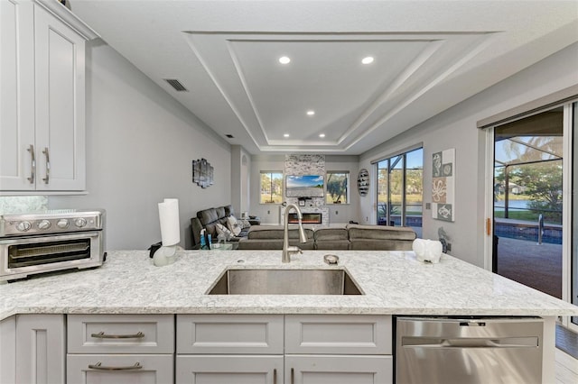 kitchen featuring visible vents, dishwasher, a sink, open floor plan, and a tray ceiling