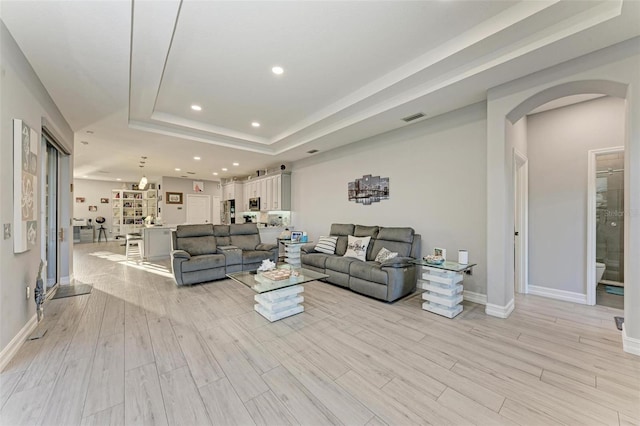 living room with visible vents, recessed lighting, a raised ceiling, arched walkways, and light wood-style floors