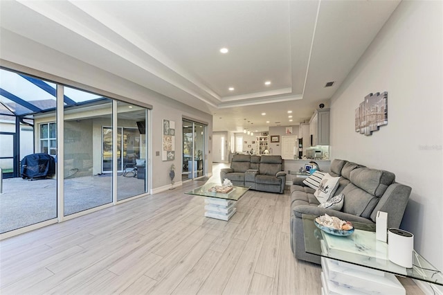 living room featuring recessed lighting, baseboards, a raised ceiling, light wood-style floors, and visible vents