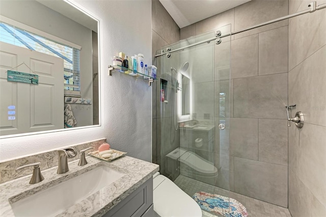bathroom with toilet, vanity, a textured wall, and a shower stall