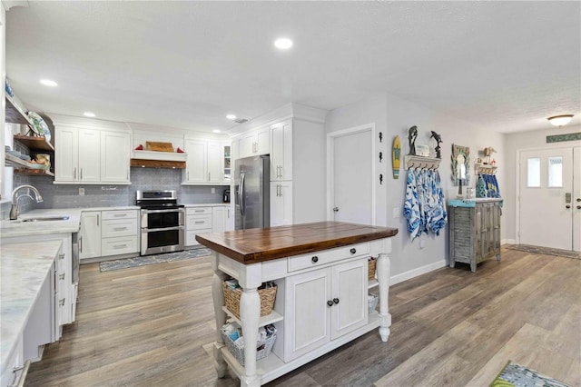 kitchen featuring appliances with stainless steel finishes, sink, light hardwood / wood-style flooring, white cabinets, and butcher block countertops