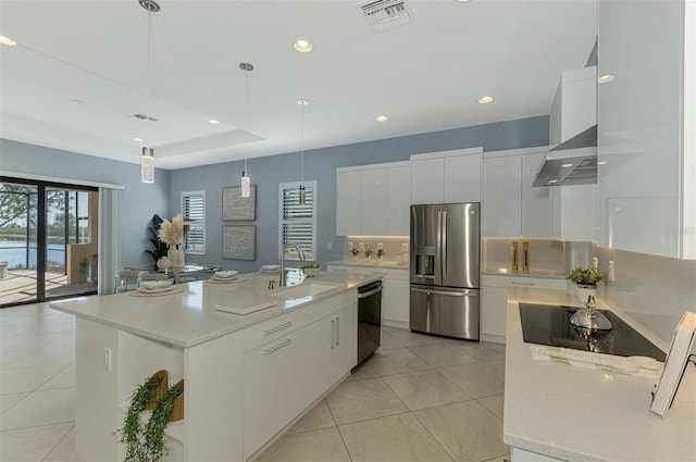 kitchen featuring stainless steel appliances, a kitchen island with sink, sink, wall chimney range hood, and decorative light fixtures