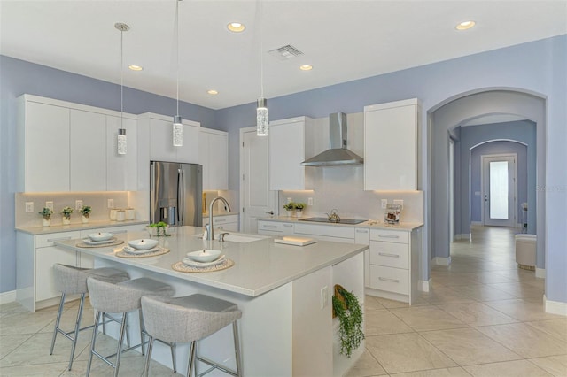 kitchen featuring a center island with sink, white cabinets, sink, wall chimney exhaust hood, and stainless steel fridge with ice dispenser