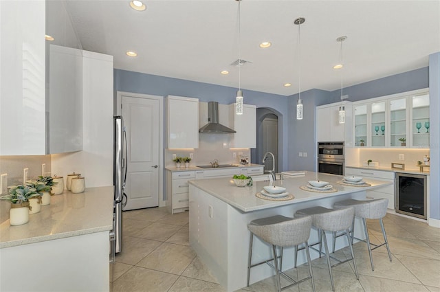 kitchen featuring white cabinetry, wall chimney range hood, hanging light fixtures, and beverage cooler