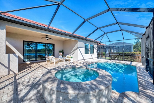 view of swimming pool with glass enclosure, ceiling fan, a patio, and an in ground hot tub